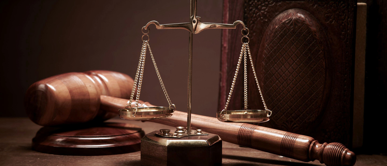 The scales of justice, a gavel, and a book sitting on a table.